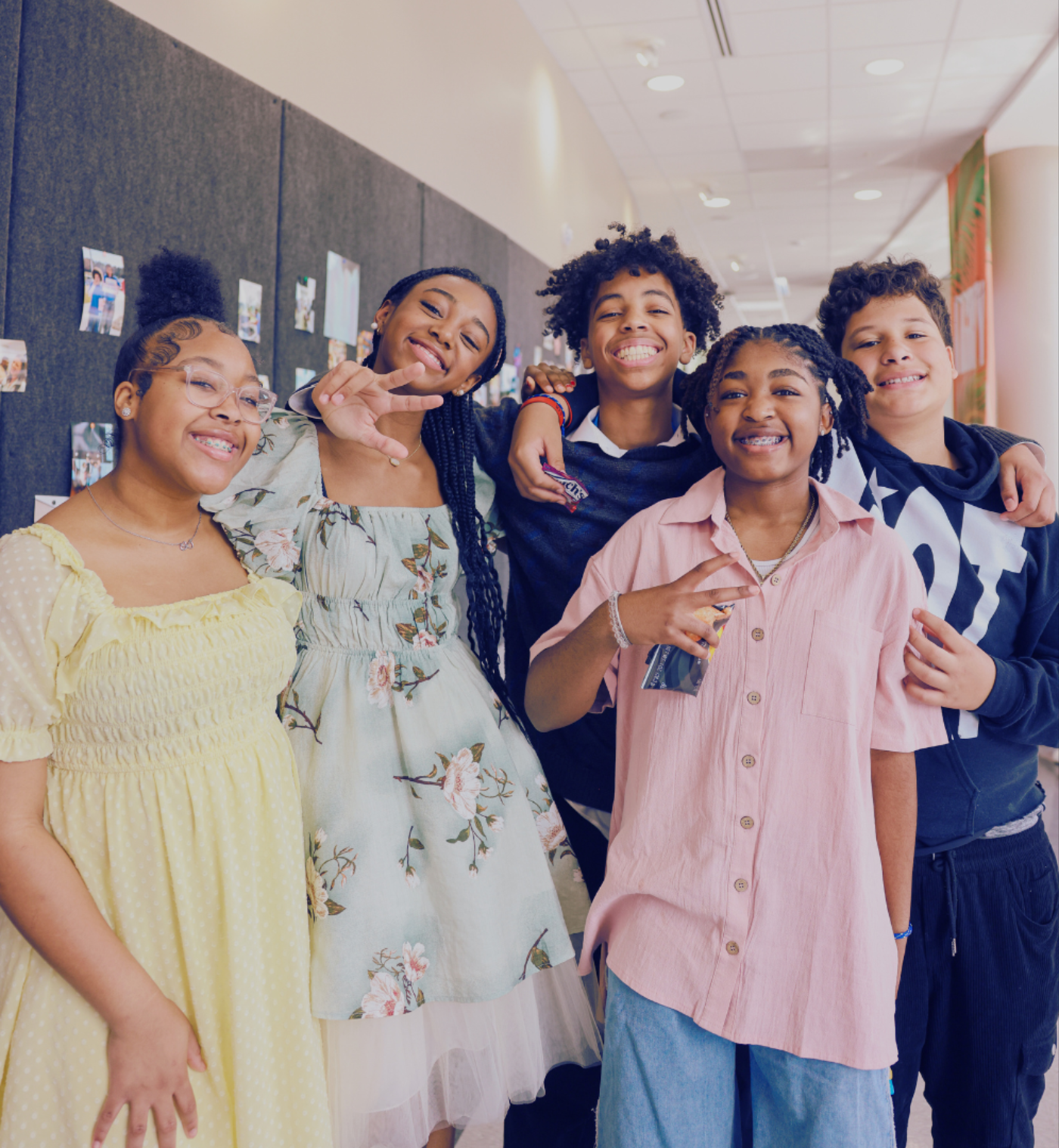 Five young teenagers together in a hallway, arms around each other